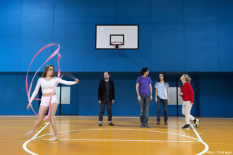 Quatre comédiens dans un gymnase et une gymnaste sur un terrain de basket. © Marc Domage